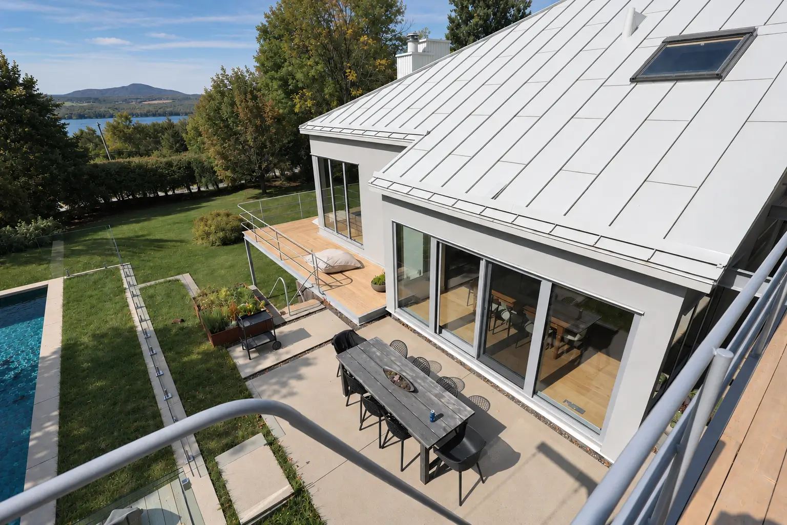 View from an upper walkway over the white metal roof, sliding glass doors and terrace, with the pool, lawn and lake beyond