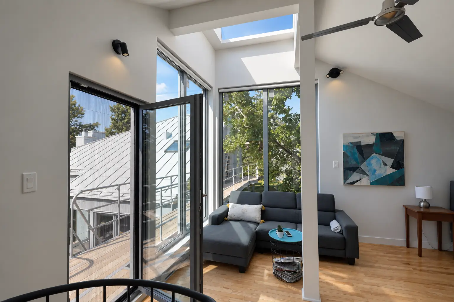 Upper-floor room with a glazed door opened inward onto an exterior walkway, tall corner glazing and a skylight above