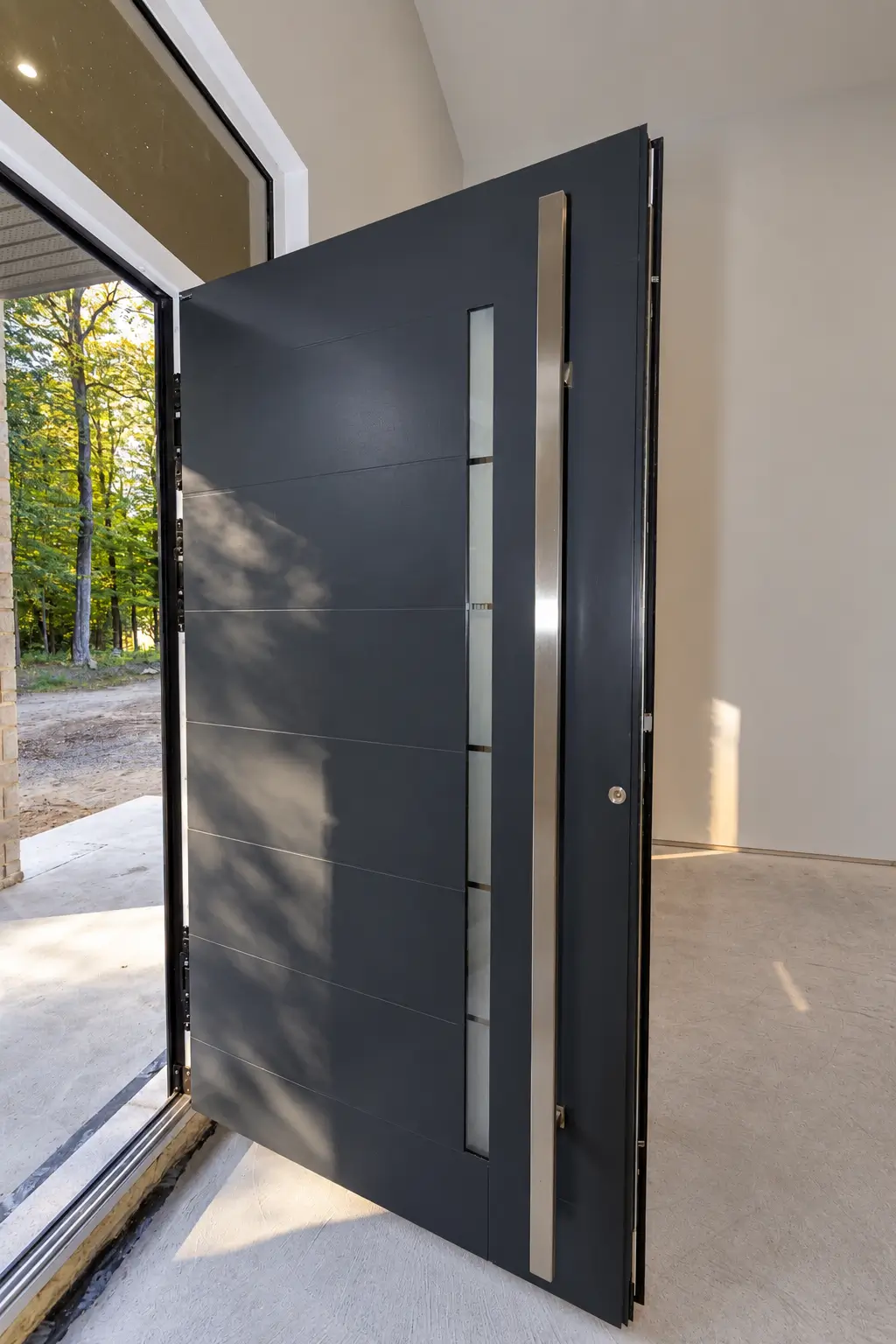Entry door standing open, showing its dark grey exterior face, a long metal pull handle and a narrow frosted glass insert