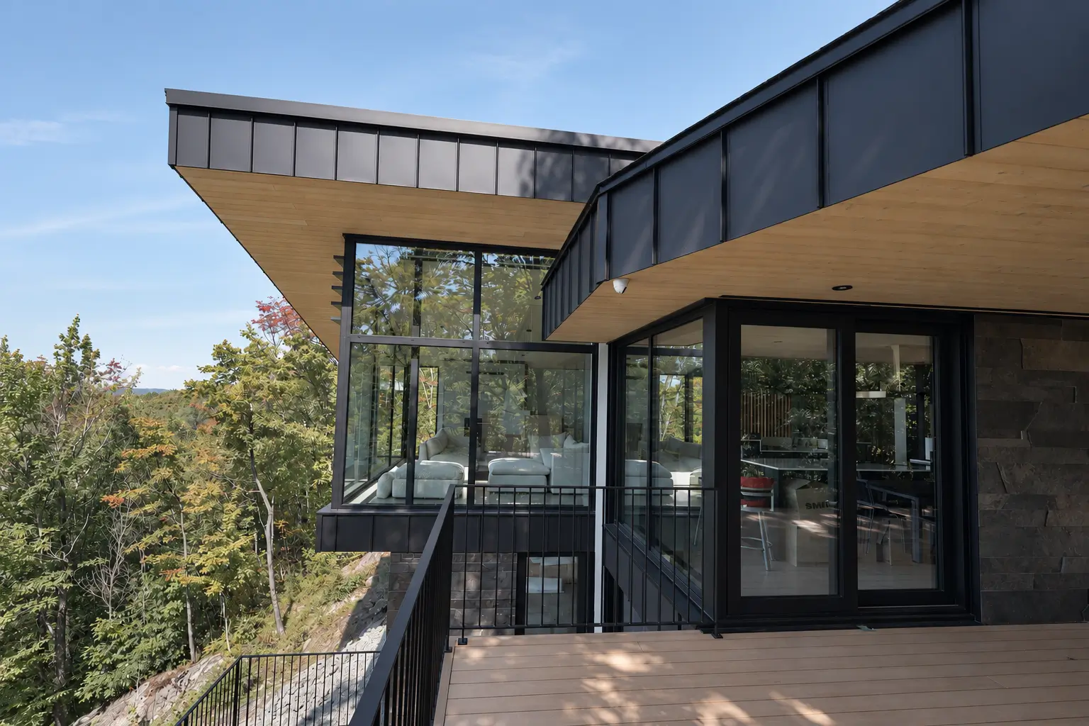 Cantilevered roof with a wood-toned soffit above a glazed corner living room and a black-framed sliding glass door opening onto a deck