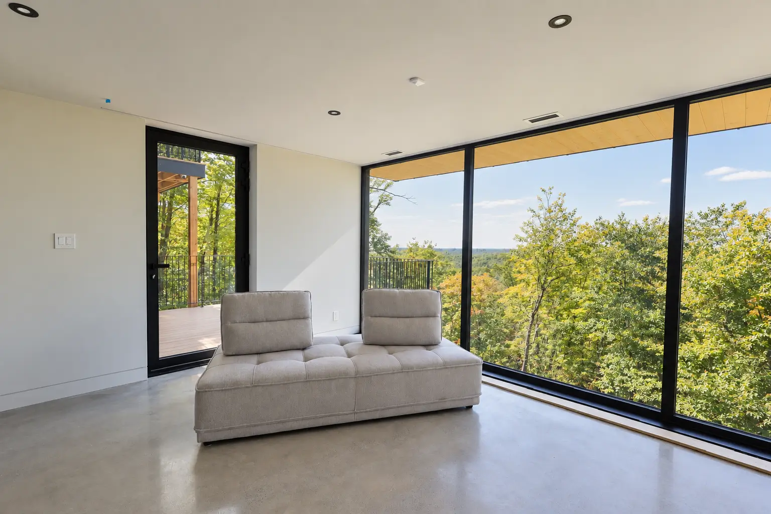 Bright room with a wall of black-framed glazing overlooking the forest and a glazed door to the deck