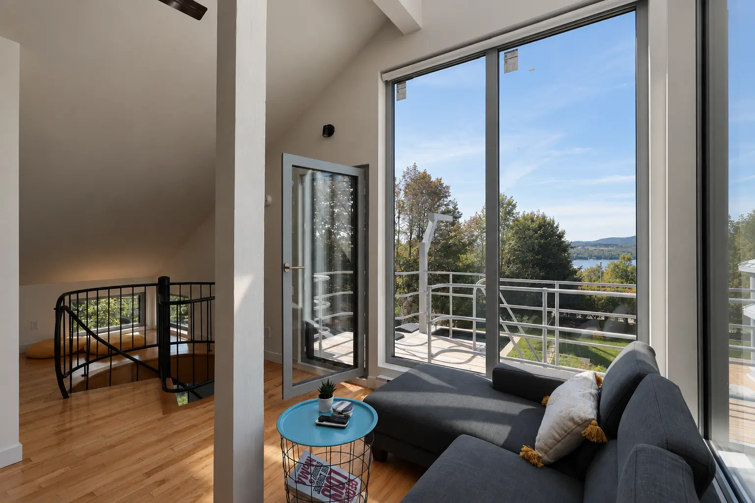 Sitting area with tall glazing framing a lake view and a glazed door opened inward to a balcony