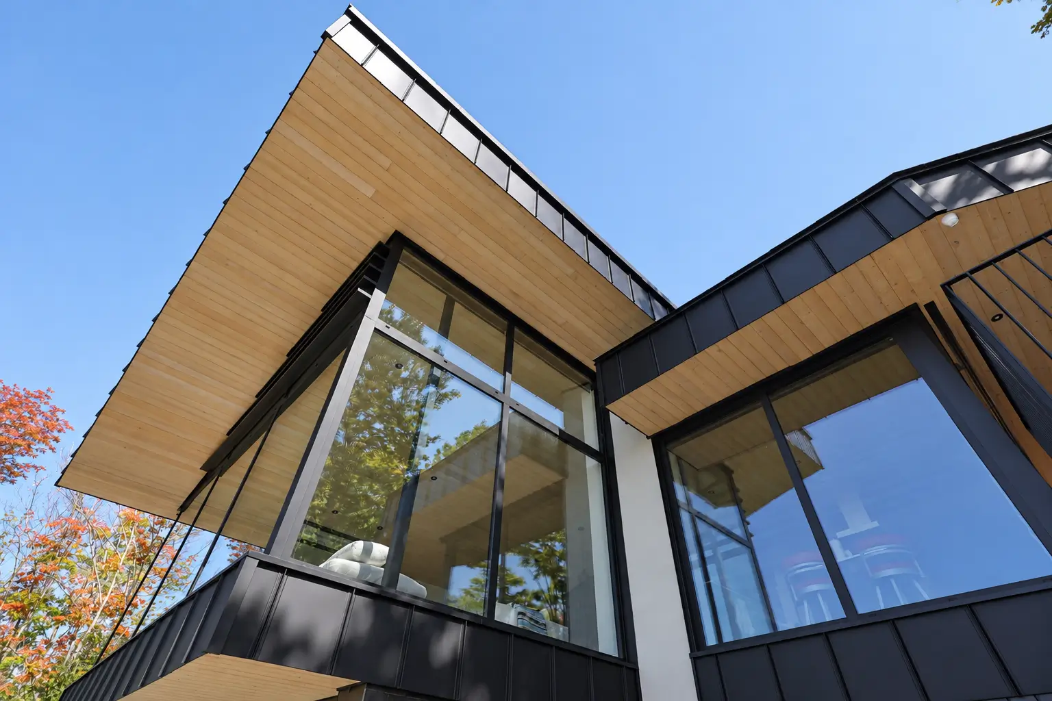 View from below of the cantilevered roof and tall black-framed corner glazing against a blue sky