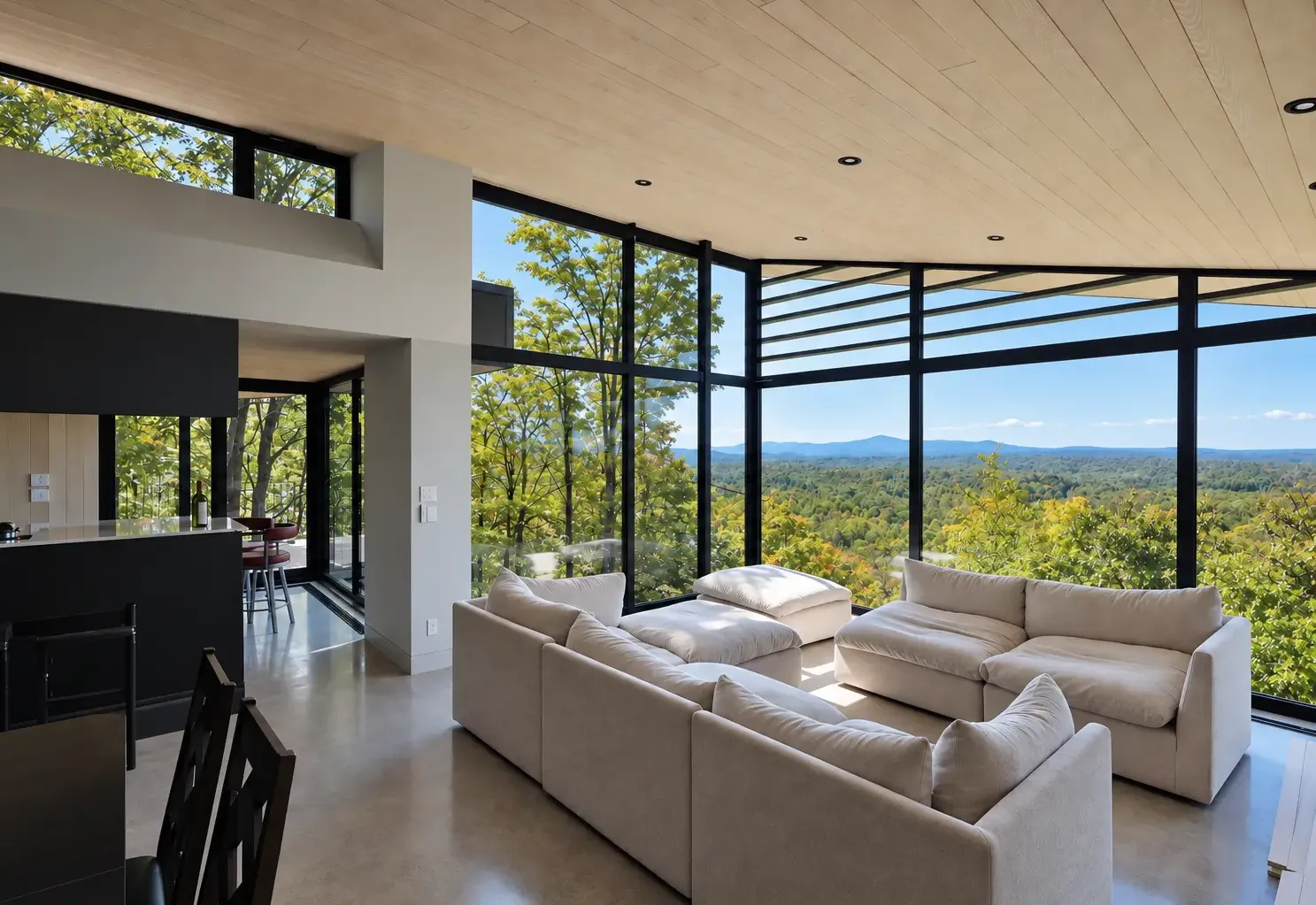 Living room with floor-to-ceiling black-framed glazing wrapping the corner and a view over treetops to distant hills