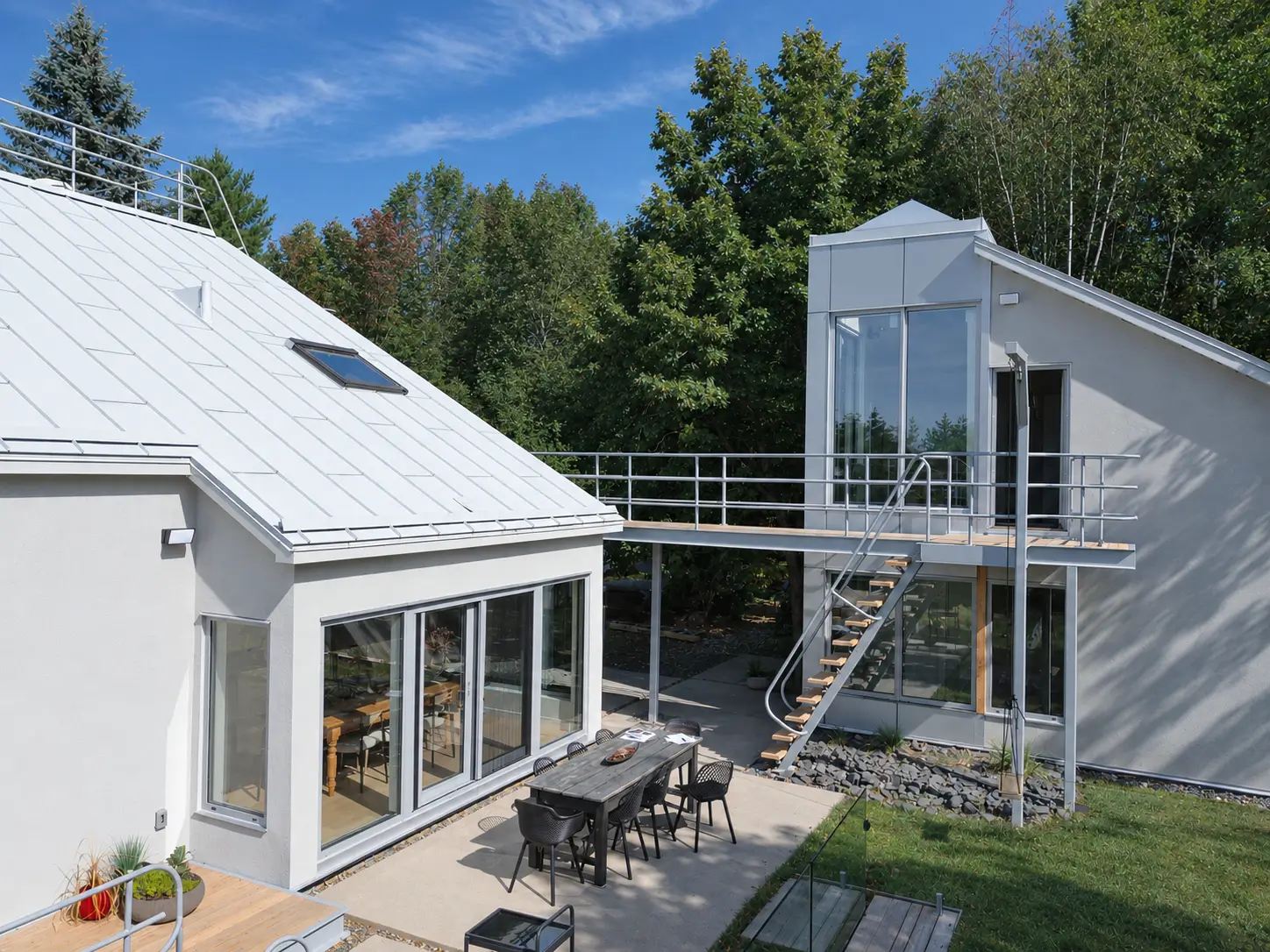 Sliding glass doors opening from a dining room onto a concrete terrace, beside a tall glazed annex reached by a footbridge and an exterior stair